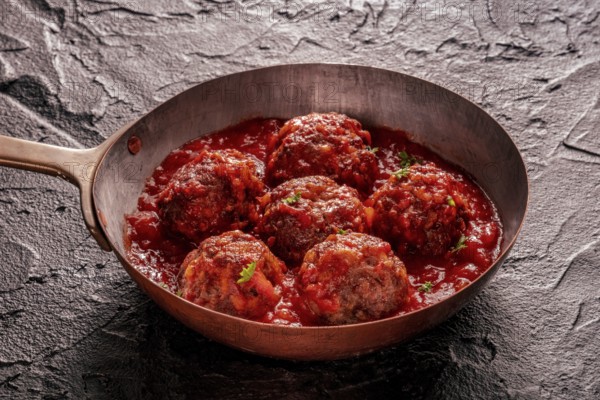 Meatballs. Beef meat balls in a pan, with parsley and tomato sauce, on a black slate background,