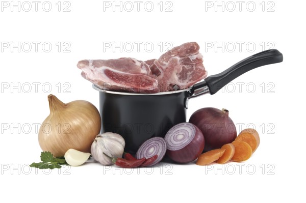 Black saucepan with pieces of raw pork inside. Around the saucepan are sliced vegetables which