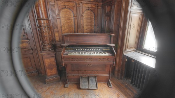 Old piano in a round window section with dark wood panelling in the background, Villa Woodstock,