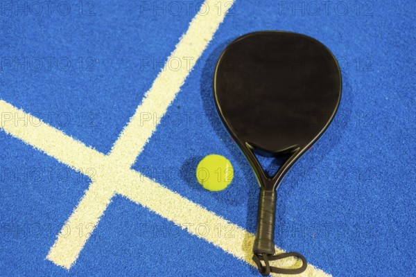 Top view of a single paddle tennis racket and ball in a blue court