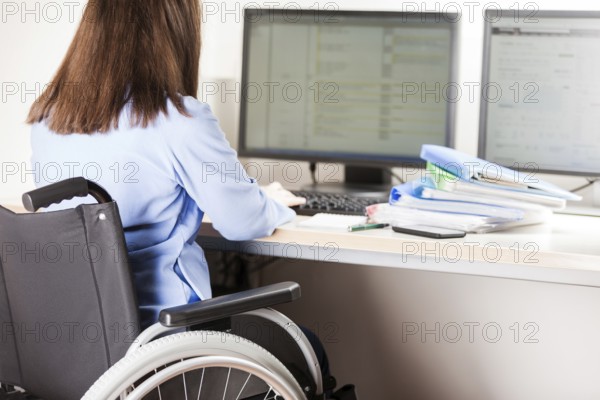 Invalid or disabled young business woman person sitting wheelchair working office desk computer