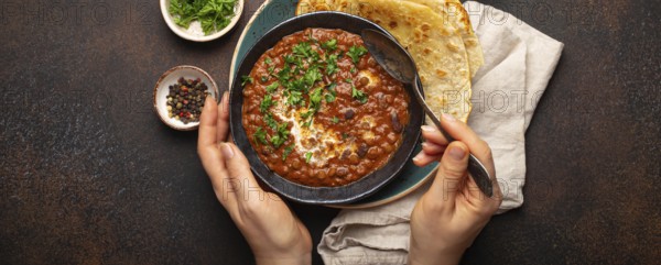 Female hands holding a bowl and eating traditional Indian Punjabi dish Dal makhani with lentils and