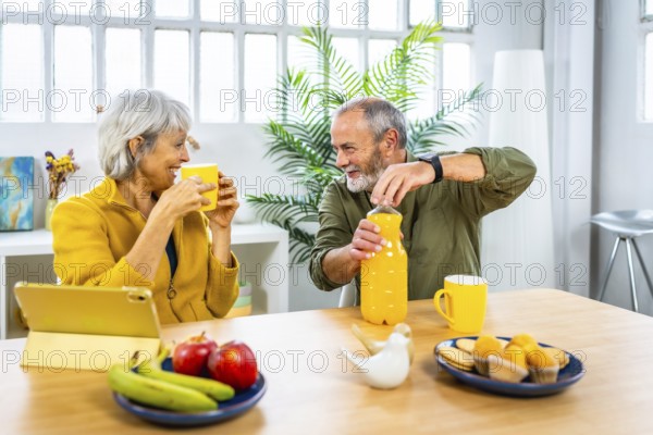 Senior couple enjoying healthy breakfast at home using tablet and talking together