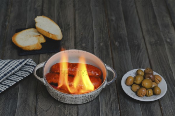 Typical spanish tapa, chorizo al infierno in ceramic casserole accompanied by bread and olives