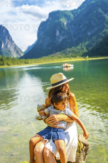 Mother embracing her son while sitting on a tree stump by the shore of lake dobbiaco, surrounded by