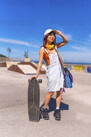 Asian woman holding a skateboard and adjusting her cap standing on a skateboard park