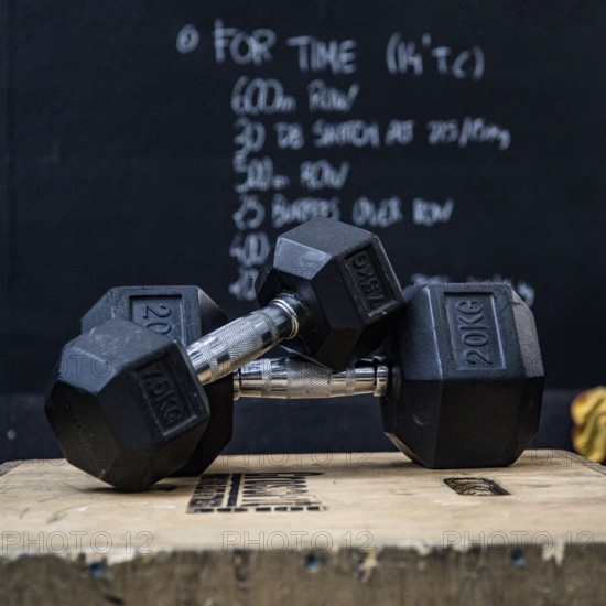 Closeup of two dumbbells on a wooden box in front of blackboard at the gym. Wod, workout of the day