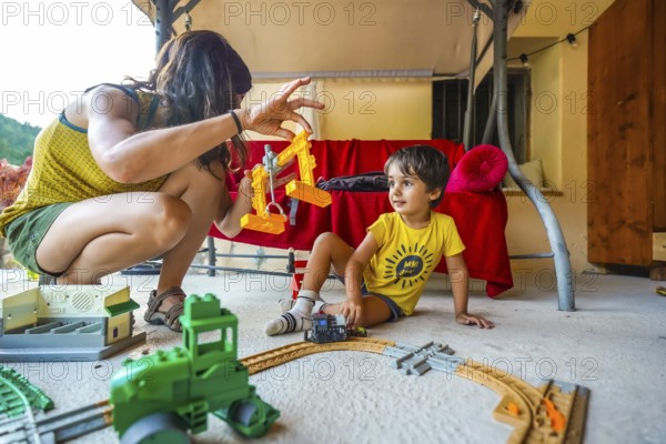 Mother and son enjoying quality time together, playing with a toy train and crane on a summer day