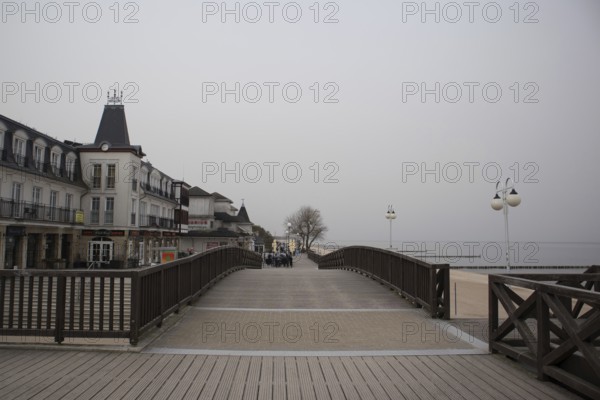 Overcast day on a boardwalk with people walking near waterfront buildings and street lamps, Mielno,