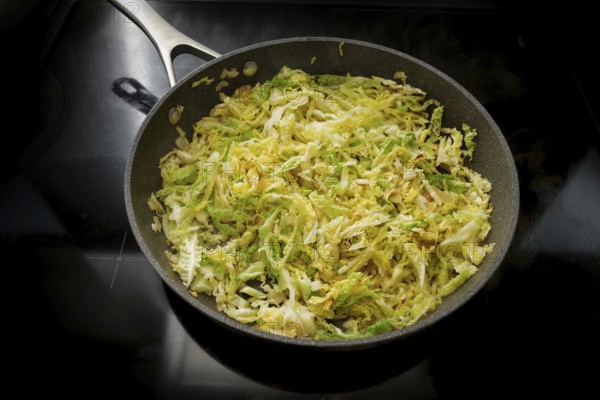 Savoy cabbage in a frying pan on the black stove, cooking at home with healthy winter vegetables,