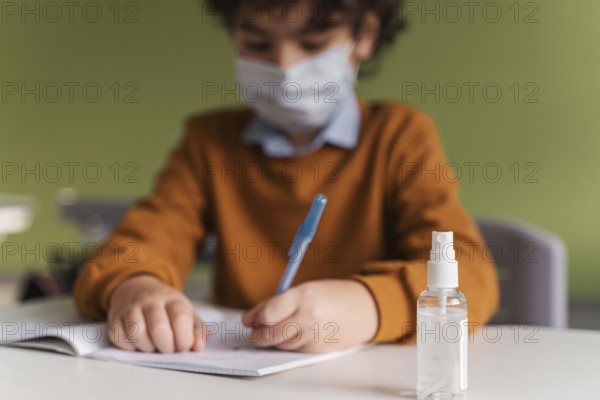 Front view child with medical mask class with bottle hand sanitizer desk