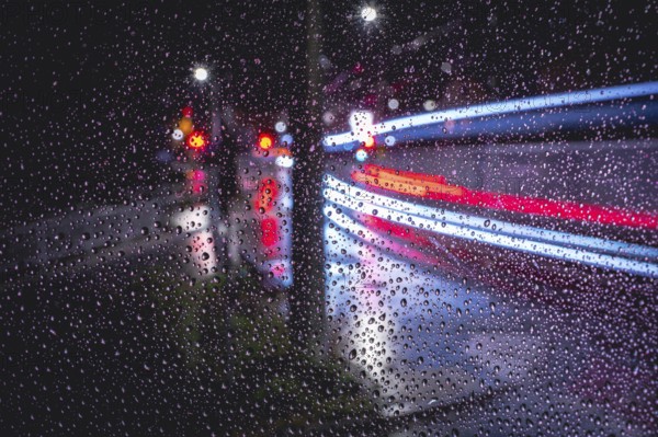 Rainy window pane with blurred light traces of passing vehicles in the dark, urban atmosphere,