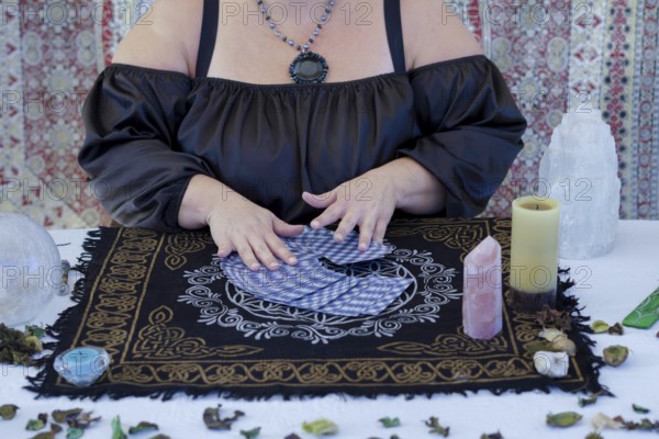 Hands of an unrecognizable fortune-teller woman dressed in black sitting at her table reading tarot