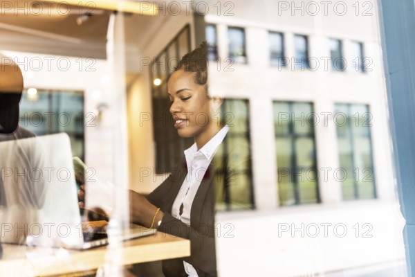 Views from outside the window of a latin businesswoman using smartphone working in a cafeteria
