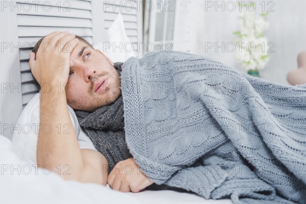 Young man lying bed with headache fever touching his forehead