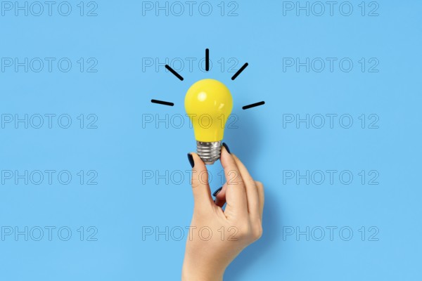Female hand hold yellow light bulb on blue background. Creative idea, innovation, brainstorming