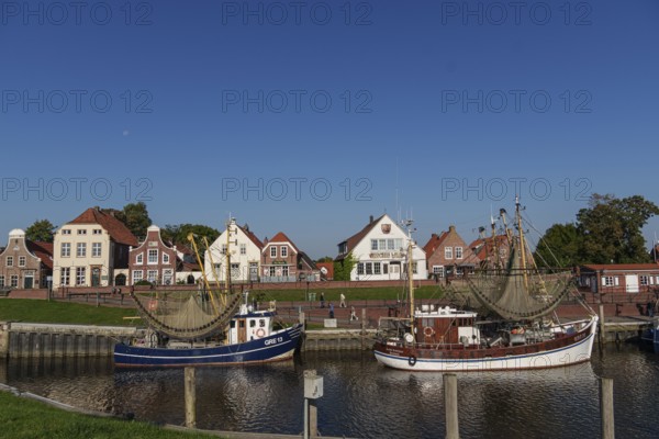 A quiet harbour with two boats and picturesque brick houses under a clear blue sky, Greetsiel, East