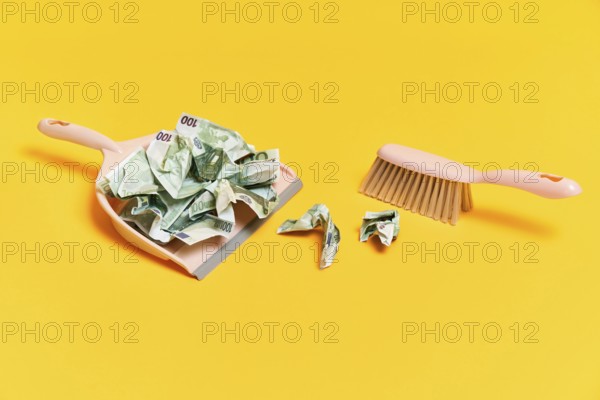 Creative layout with dustpan, hand brooms and crumpled money dollar bills on yellow background.