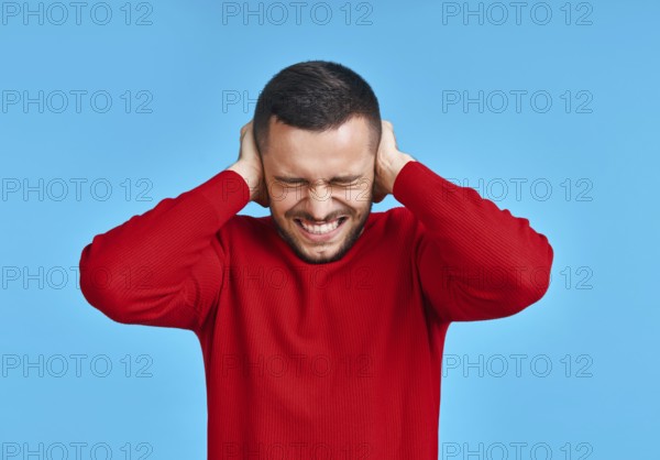 Handsome man covering his ears with hands afraid to hear bad news isolated on blue background.