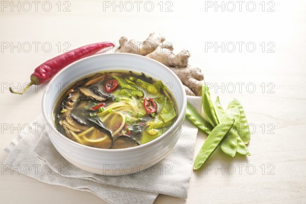 Spicy Asian vegetable soup with noodles, miso, nori seaweed, ginger and chili in a bowl on a wooden