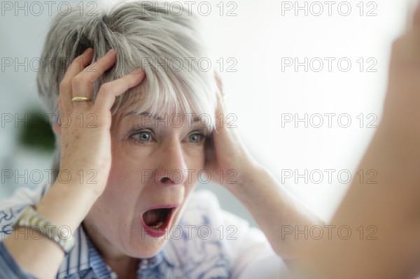 An elderly lady looks in the mirror in horror and ruffles her hair