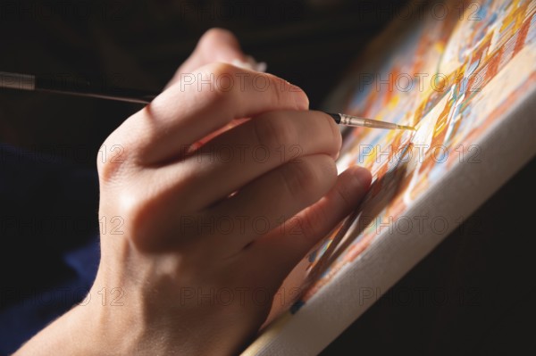 Close-up of a female artist's hand painting with watercolors color on canvas with a brush in a dark