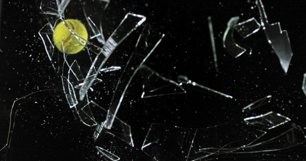 Tennis Ball breaking Pane of Glass against Black Background