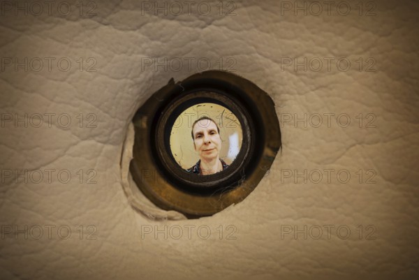 Woman seen out of focus through the old dirty peephole of the front door of a dark apartment