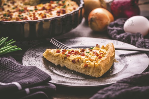 Piece of homemade onion tart or pie with bacon and chive on wooden background