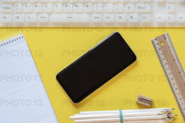 Office desk above view with a black smartphone, white keyboard, and office props