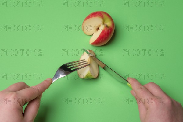 Top view of a woman hands with cutlery, cutting a slice of apple on a green background. Ready to