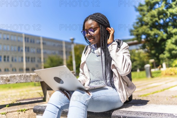 African female student with braided long hair using laptop outside the campus in a sunny day