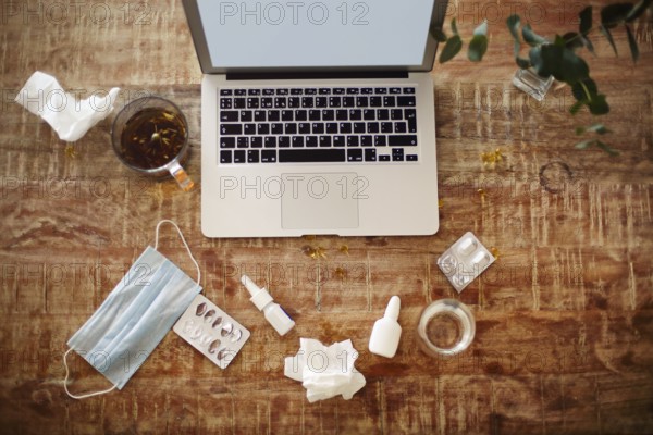 From above various drugs and medical mask placed on table near plant twigs in vase and laptop with