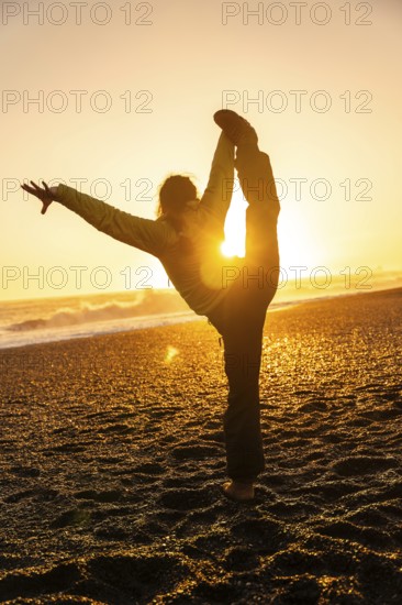A woman is doing a yoga pose on a beach at sunset. Concept of relaxation and tranquility, as the