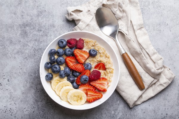 Oatmeal porridge with fruit and berries in bowl with spoon on white wooden background table top