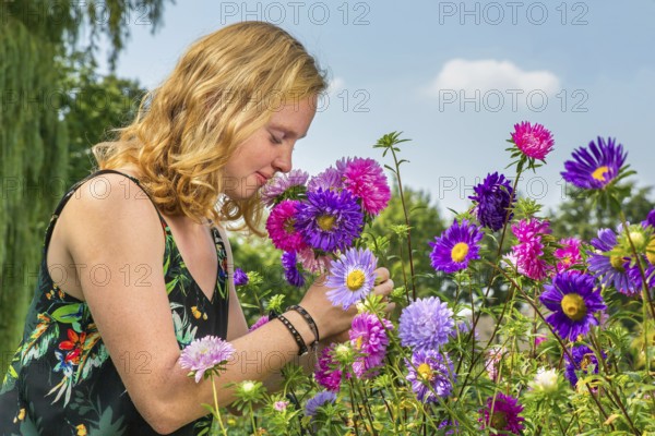 Young dutch redhead woman smelling summer flowers in garden