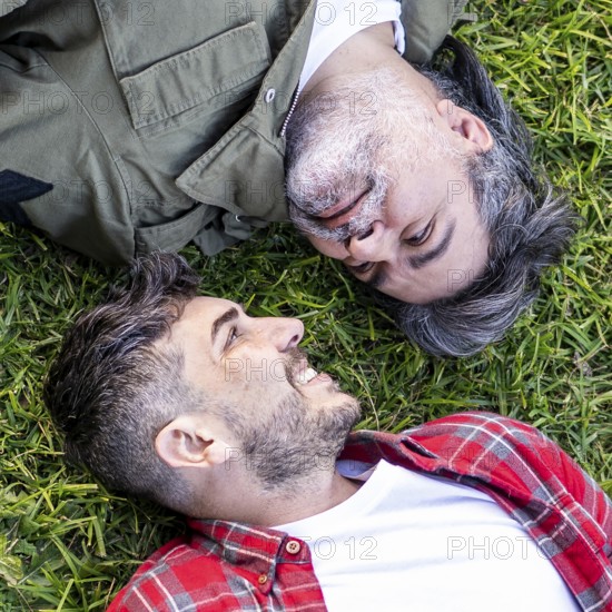 Top view of a Hispanic gay couple lying on the grass while looking to each other