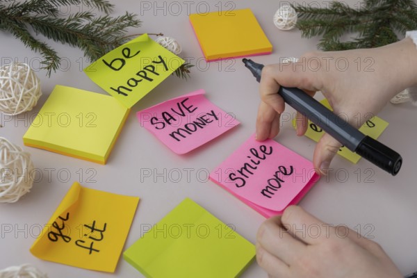 Unrecognizable woman writing new year's resolutions on colorful sticky notes. Making promises for