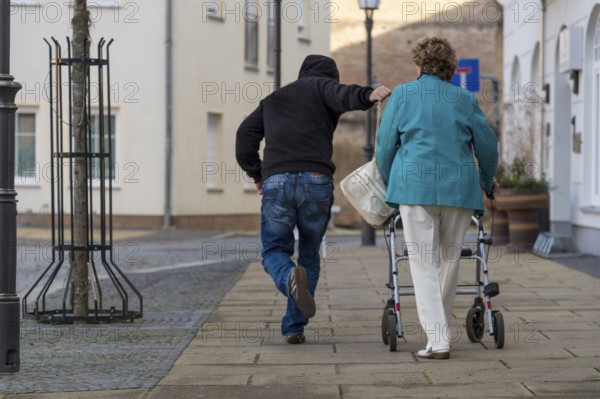 A man snatches a senior citizen's handbag from her shoulder as she passes by. Rear view