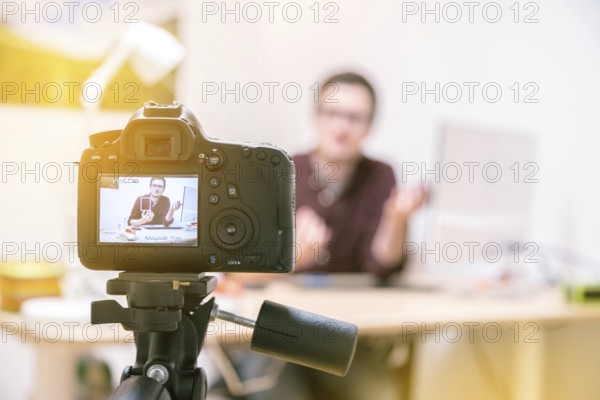 Camera on a tripod filming a blogger at home sitting on his workspace