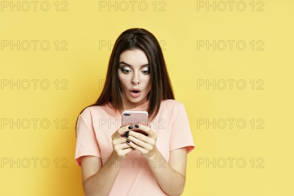 Portrait of a shocked pretty millennial hipster girl using mobile phone isolated over yellow