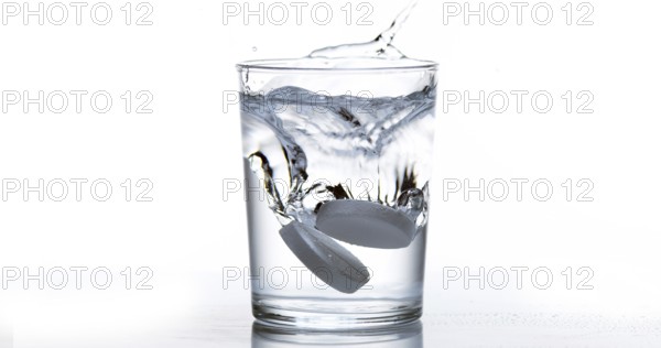 Tablets Falling and Dissolving into a Glass of Water against White Background