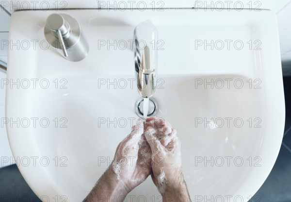 top view of person thoroughly washing hands at bathroom sink with soap and hot water, hygiene