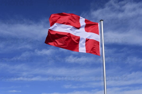 The flag of Denmark flutters in the wind against a blue cloudless sky
