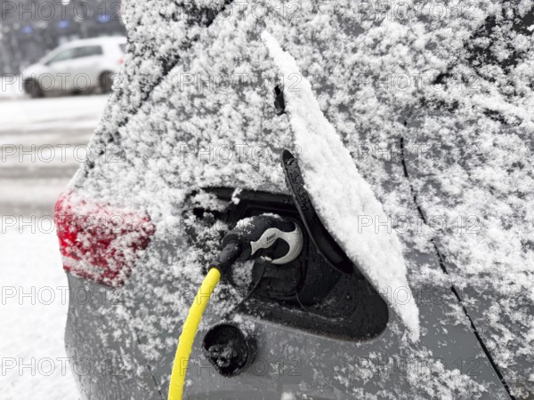 Charging an electric vehicle in winter. A yellow charging cable is connected to the car's charging