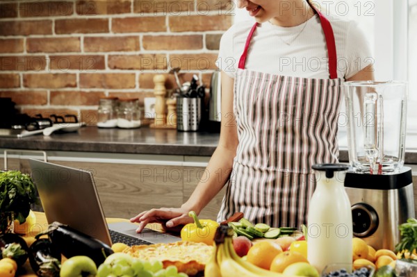 Woman using laptop at home kitchen. Girl touching touchpad with hand, searching for a recipe. Chef