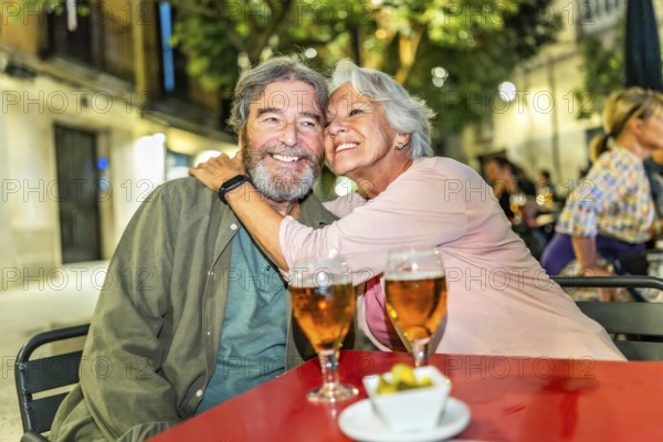 Senior happy couple embracing drinking beer in sidewalk bar in the city