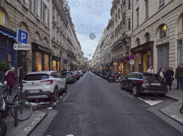 A busy city street at dusk with parked cars and pedestrians, Rue de L'Odeon .Paris