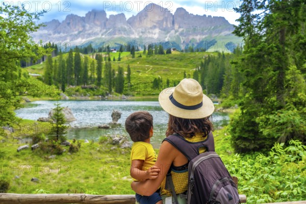 Mother carrying her son while enjoying breathtaking views of emerald waters at lake carezza,