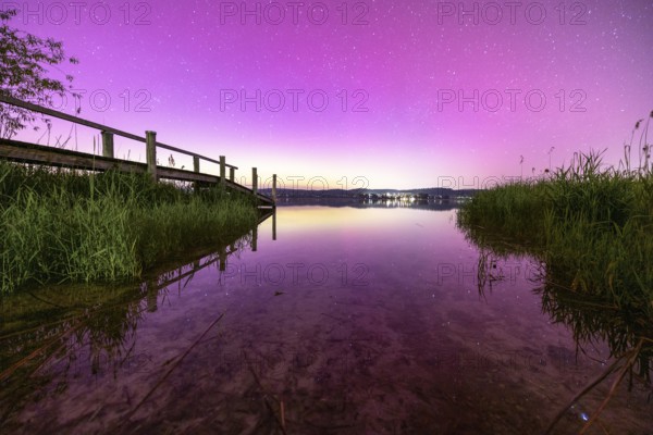 View of a calm lake with pink sky and starry sky with aurora borealis, Reichenau, Lake Constance,